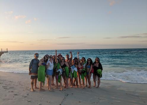 Group of students standing on the beach with waves behind them and smiling